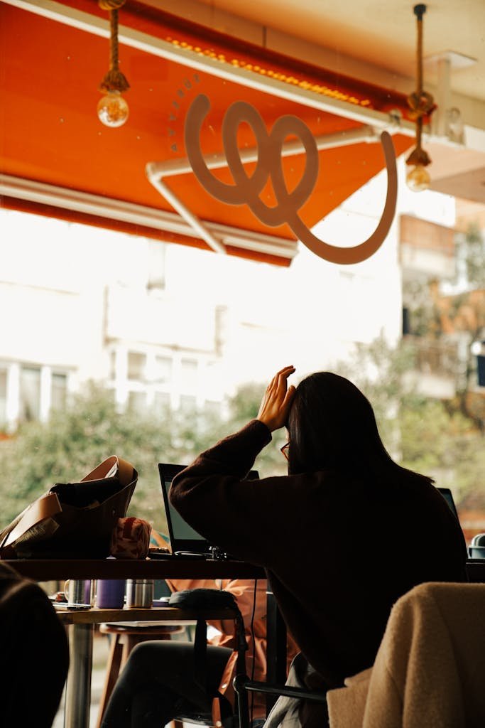Person working on a laptop in a cozy cafe, bent over with focused attention.